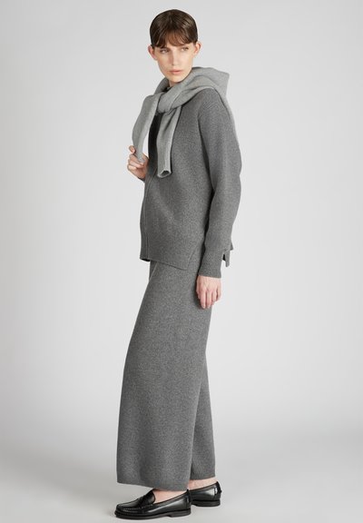 Grauer Strickpullover mit Kapuze, kombiniert mit einem passenden langen, fließenden Rock. Schwarze Loafer runden das Outfit ab. Weicher, glatter Stoff durchgehend.