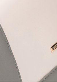 Borsa a due tonalità con la parte superiore liscia bianca e la base grigia texturizzata, dotata di accessori dorati con dettaglio del logo inciso.