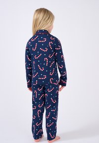 Conjunto de pijama azul marino con un patrón de bastones de caramelo en blanco y rojo, con corazones verdes; camiseta de manga larga y pantalones a juego en una tela suave.