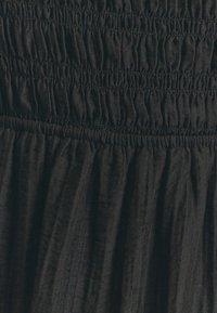 Indumento nero caratterizzato da un design arricciato e testurizzato con pieghe. Il tessuto sembra leggero con una finitura morbida e leggermente stropicciata.