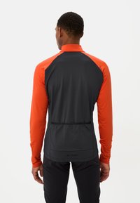 Veste de sport pour homme avec un corps noir et des manches orange, texture lisse, col zippé et poche arrière avec un logo en bas.