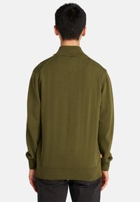 Olivgrön stickad tröja med krage, ribbade ärm- och fållkanter. Har en sömlös axeldesign och en liten etikett på vänster sida.