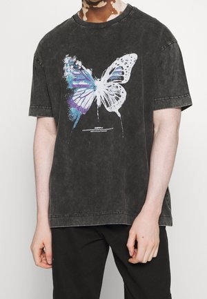T-shirt en coton noir surdimensionné avec un grand imprimé graphique d'un papillon multicolore sur le devant, avec une finition décolorée et usée.