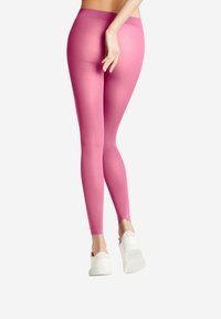 Leggings rosa con una texture liscia e elastica, vita alta e design aderente, abbinati a calzature bianche.
