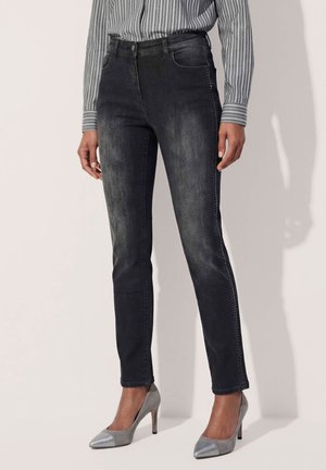 Frau trägt schwarze ausgebleichte Skinny-Jeans, gestreiftes Langarmshirt und graue spitze High Heels, steht vor hellem Hintergrund.