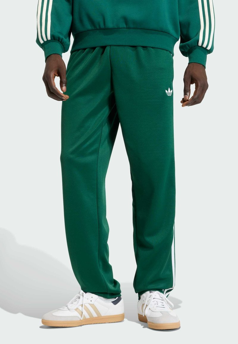 Zelené sportovní kalhoty s volným střihem, zdobené bílými bočními pruhy a vyšitým logem. Kombinované s bílými teniskami a gumovou podrážkou.