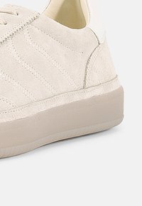 Ανοιχτό μπεζ σνίκερ από σουέντ με υφασμάτινες επενδύσεις, στρογγυλεμένη μύτη και λαστιχένια σόλα. Διαθέτει διακριτικές ραφές και επενδεδυμένο γιακά.