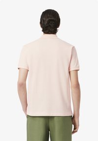 Ljusrosa kortärmad polo med krage, slätt tyg och ribbade ärmslut, parat med gröna shorts. Inga synliga mönster.