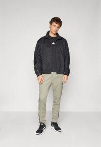 Μαύρο σακάκι με σχέδιο και φερμουάρ, μαύρη μπλούζα, ανοιχτοπράσινο παντελόνι με μαύρες ρίγες και μαύρα αθλητικά παπούτσια. Απλός σχεδιασμός και αθλητική εφαρμογή.