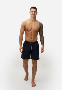 Marine zwembroek met een trekkoord in de taille en zijzakken, gemaakt van lichtgewicht materiaal, tentoongesteld op een staande mannelijke model.
