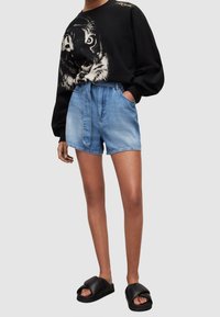 Černá mikina s grafikou tygra, modré džínové kraťasy s vysokým pasem a páskem na zavazování, a černé pantofle na skluz.