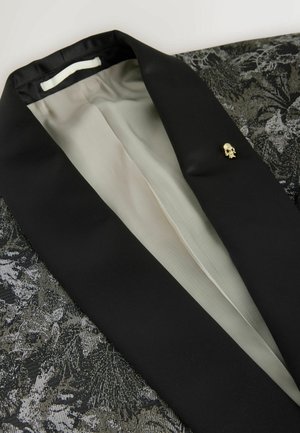 Blazer negru cu un material texturat și un model floral. Detalii notabile includ un ac cu craniu auriu și o căptușeală interioară netedă.