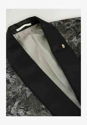 Zwarte blazer met een textuurstof en een bloemenpatroon. Opvallende details zijn een gouden schedelspeld en een soepele voering.