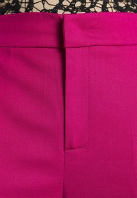 Vêtement magenta vif avec une ceinture et une fermeture avant cachée, surmonté d'un détail en tissu de dentelle noire au bord supérieur.