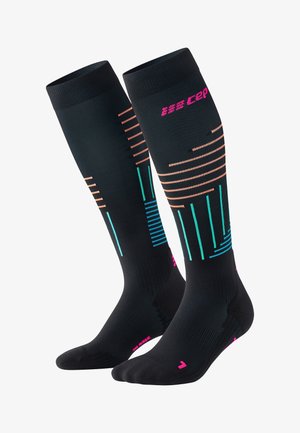 Kompressionsstrümpfe in Schwarz mit geometrischen Mustern in Pink, Orange und Türkis. Hergestellt aus strukturiertem, elastischem Material für Unterstützung. Knielanges Design.