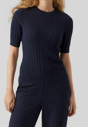 Femme portant un haut en maille à manches courtes bleu marine avec un motif vertical texturé et un pantalon bleu marine à fines rayures.