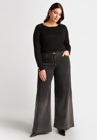 Blusa negra de manga larga y jeans negros de pierna ancha, con detalles de botones dorados en las mangas, textura suave y corte relajado.