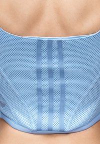 Κοντινό πλάνο του πάνω μέρους της πλάτης ενός ατόμου που φοράει έναν ανοιχτό μπλε αναπνεύσιμο νάρθηκα πλάτης με τρεις κάθετες λωρίδες υποστήριξης.