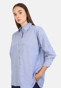 Camicia a righe blu chiaro e bianca con bottoni, caratterizzata da un colletto classico, maniche lunghe e una vestibilità rilassata con fessure laterali.
