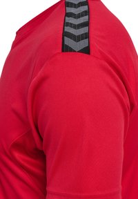Camiseta atlética roja con una textura suave y un acento negro con patrón a lo largo del hombro para aportar detalle y contraste.