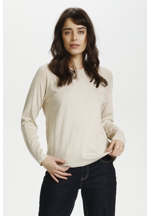 Beige Longsleeve-Jersey-Oberteil mit rundem Halsausschnitt und gerippten Bündchen, kombiniert mit dunklen Jeans. Weiche Textur, figurbetonter Schnitt.