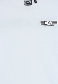 Hvit EA7 Emporio Armani t-skjorte med svart og hvitt logo trykket på brystet og merkeetikett inni kragen.
