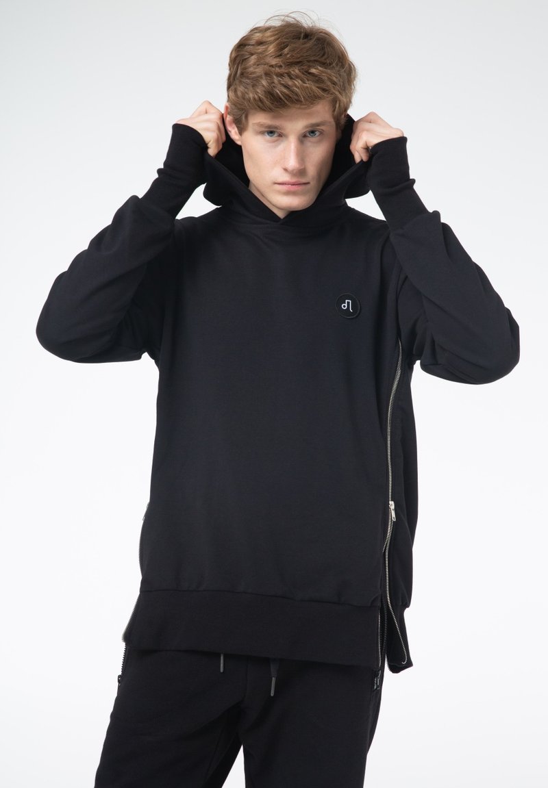 Czarna bluza z kapturem, wykonana z miękkiego materiału, z wysokim kołnierzem, zamknięciem na zamek i okrągłym logo na klatce piersiowej. Bezszwowy, luźny krój.