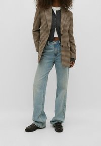 Blazer à carreaux marron porté sur un cardigan gris, associé à un jean taille haute bleu clair et des mocassins noirs. Tissus texturés et coupe décontractée.