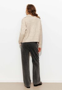 Pull beige texturé à manches longues, assorti à un pantalon large gris foncé. Les deux vêtements présentent une coupe décontractée, mettant en avant le confort.