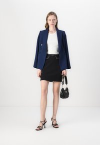 Marineblazer med store knapper, hvid ribbet top, sort mini-nederdel med bælte, stroppede sorte hæle og en kviltet sort håndtaske.