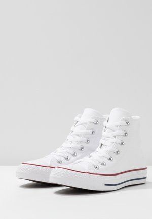 Para białych, wysokich sneakersów wykonanych z płótna z białymi sznurówkami, metalowymi oczkami oraz czerwonymi i niebieskimi paskami na gumowej podeszwie.