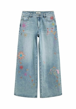 Jean large bleu clair avec des étoiles brodées colorées, des motifs célestes, un oiseau et une licorne sur les jambes avant, fermeture par bouton et zip.