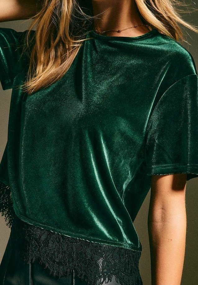 Femme portant un haut court en velours vert foncé avec une bordure en dentelle noire à l'ourlet et un délicat collier en or.