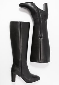 Botas de cuero negro hasta la rodilla con punta afilada y un tacón alto en bloque. Presentan un cierre de cremallera en la parte posterior y detalles de costura vertical.