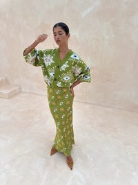 Cardigan vert avec motifs d'œil, associé à une jupe assortie à motifs. La tenue comprend des manches surdimensionnées et des talons marron pointus ornés de clous.