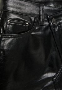 Sorte denimjeans med en blank finish, der har en forlomme, metalnitter og en struktureret overflade med synlige syningsdetaljer.