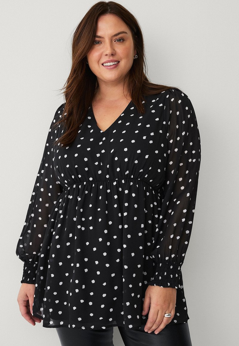 Zwarte blouse met lange doorschijnende mouwen, V-hals, elastische tailleband en een patroon van witte stippen. Gladde textuur met plooidetails bij de manchetten.
