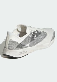 Zapatilla deportiva blanca con detalles en negro, con parte superior texturizada, puntera redonda, cierre con cordones y suela acolchada.