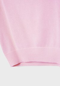 Tissu tricoté rose doux avec un ourlet côtelé, montrant une texture fine et une couture lisse et régulière en vue rapprochée.