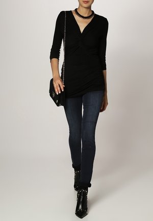 Top negro ajustado con mangas de tres cuartos, detalle fruncido y escote en V. Combinado con jeans oscuros ajustados y botas de tobillo negras con tachuelas.