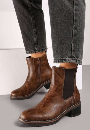 Bottes en cuir marron de cheville avec panneaux latéraux en élasthanne, petits talons carrés et détails de couture visibles. Fini texturé, bout légèrement arrondi.