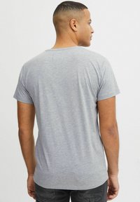 Camiseta de algodón gris con mangas cortas, cuello redondo y una textura suave. Sin patrones visibles; diseño ajustado con un dobladillo curvado.