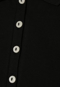 Zwarte poloshirt met een gestructureerde stof, met witte knopen aan de voorkant. Close-up details benadrukken het ontwerp van de knopen en de weving van de stof.