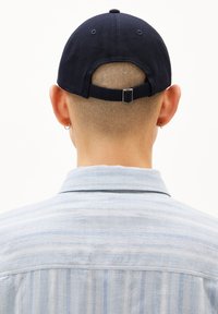 Een marineblauwe katoenen baseballcap met een verstelbare strap aan de achterkant. Draagt bij een lichtblauw gestreept shirt. Textuur van de stof is zichtbaar.
