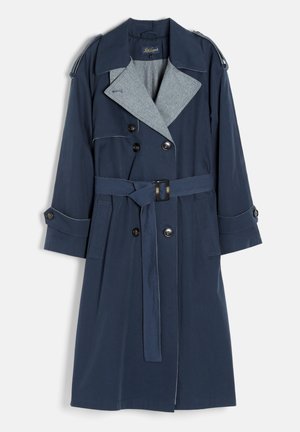 Trench-coat bleu marine avec doublure intérieure grise, boutons croisés, taille ceinturée, épaulettes aux épaules et poignets boutonnés.