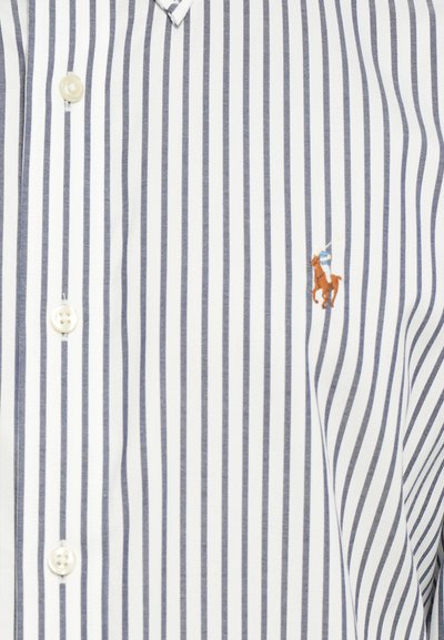 Chemise à manches longues à rayures blanches et marines, ornée d'un petit logo brodé d'un cavalier. Tissu en coton lisse avec un col classique.