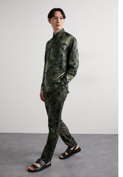 Green floral patterned shirt and matching pants, made from smooth fabric, paired with black sandals, showcasing a modern silhouette.