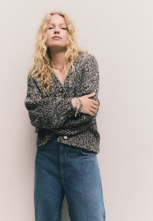 Ylisuuri harmaa neulottu neuletakki tekstuurikuvioinnilla, napitettava ja pitkähihaiset. Yhdistetty korkeavyötäröisiin sinisiin farkkuihin.