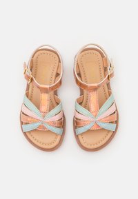 Sandalias con tiras de base marrón, que presentan tiras sintéticas en tonos rosa pastel, verde y azul, hebilla ajustable y suela acolchada.