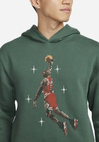 Felpa verde con un grafiche pixelato di un giocatore di basket in rosso e bianco, con scintille attorno, che mostra una posa dinamica in salto.